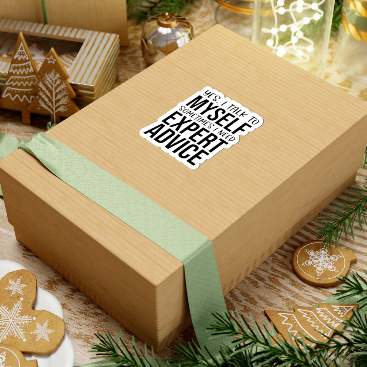 Wooden gift box with a green ribbon and humorous sticker on a festive background with cookies and lights.