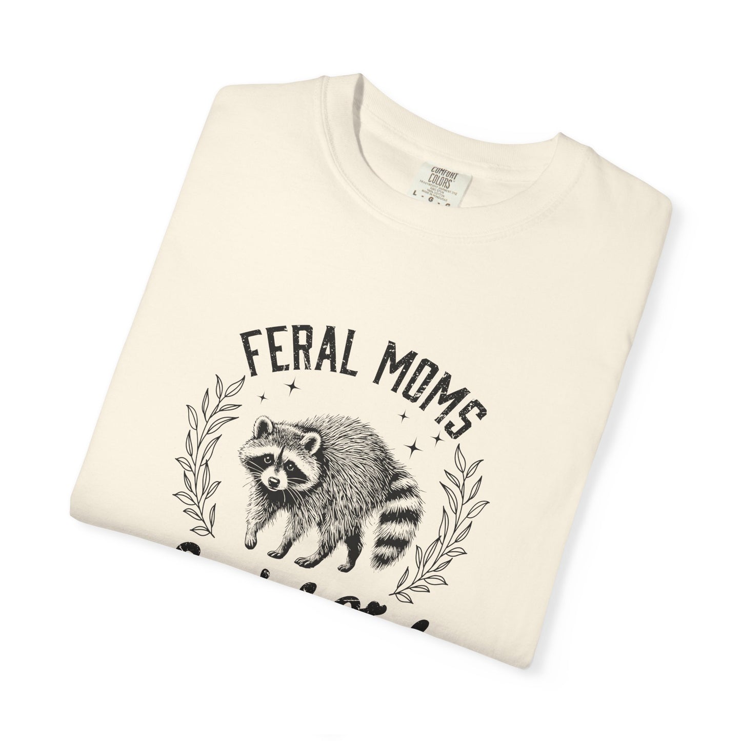 Folded t-shirt with raccoon graphic and 'Feral Moms' text on a white background